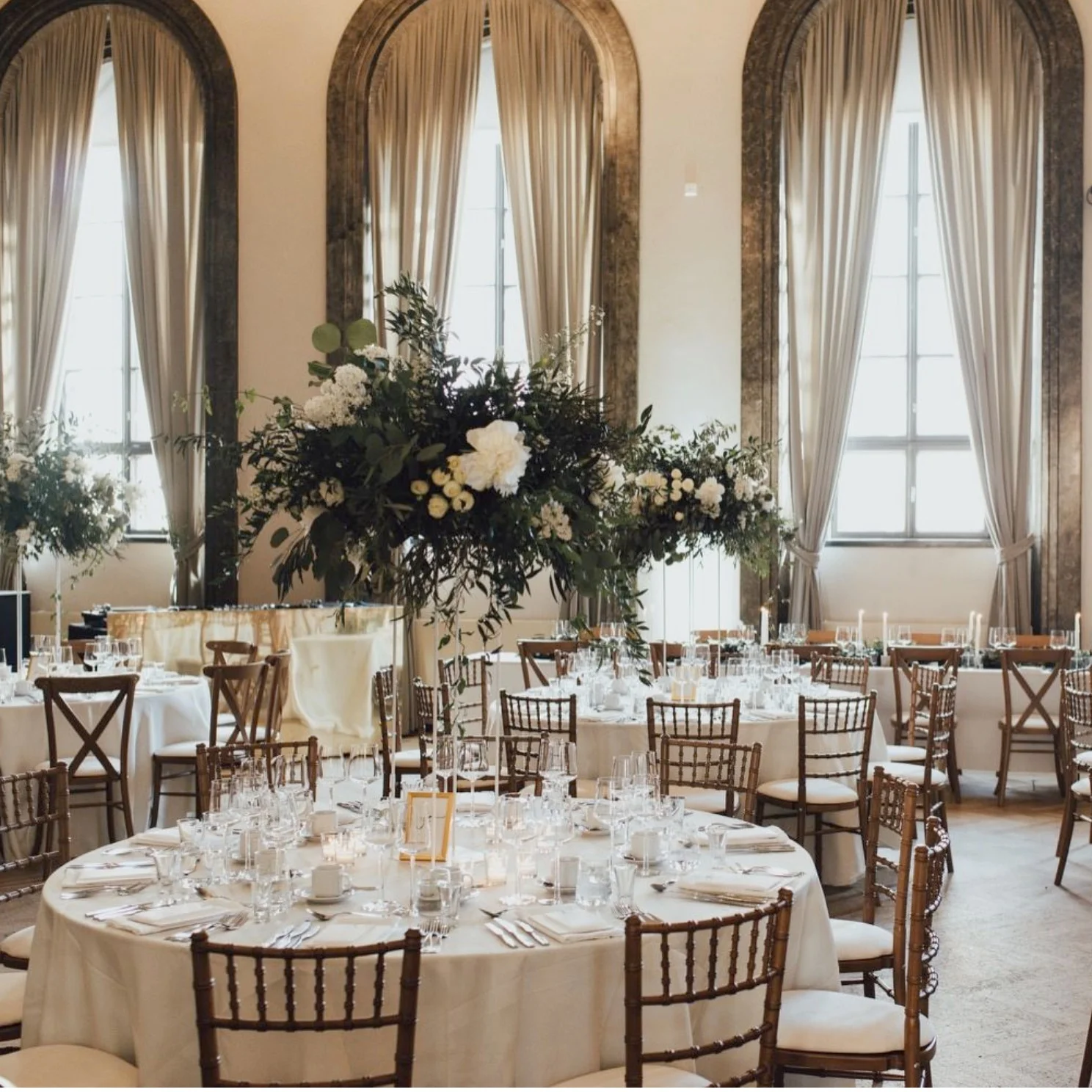 Valkoinen Sali set for dinner with round tables, white tablecloths and floral arrangements